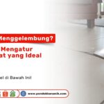 Close-up lantai keramik berwarna krem yang retak dan terangkat ke atas karena masalah pemuaian di dalam ruangan