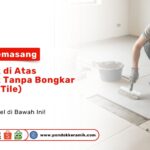 Seorang tukang menggunakan sarung tangan sedang mengoleskan semen perekat di atas lantai lama untuk memasang keramik baru